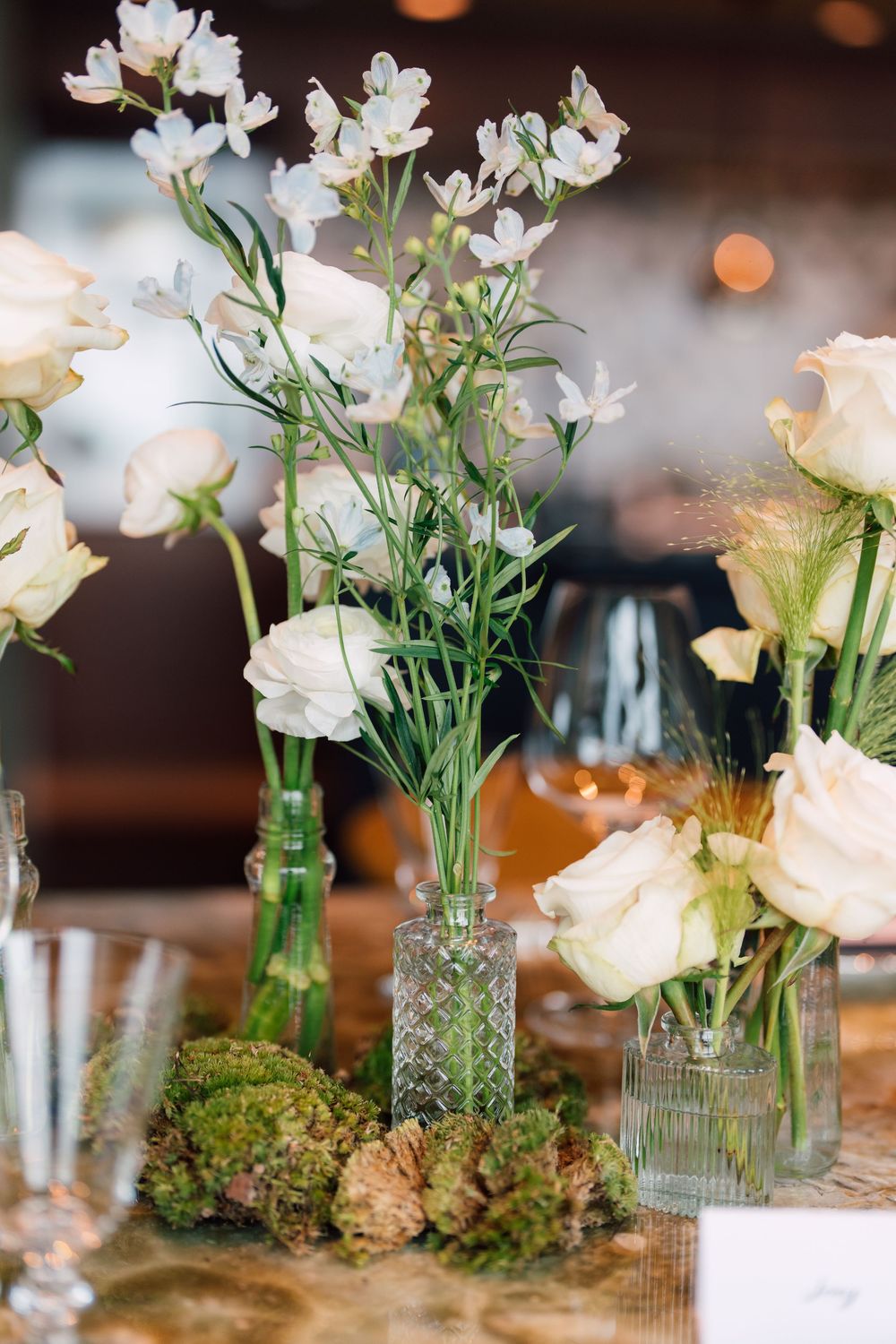 White delphinium flowers arranged in glass bud vases with moss accents create an elegant table centerpiece display.