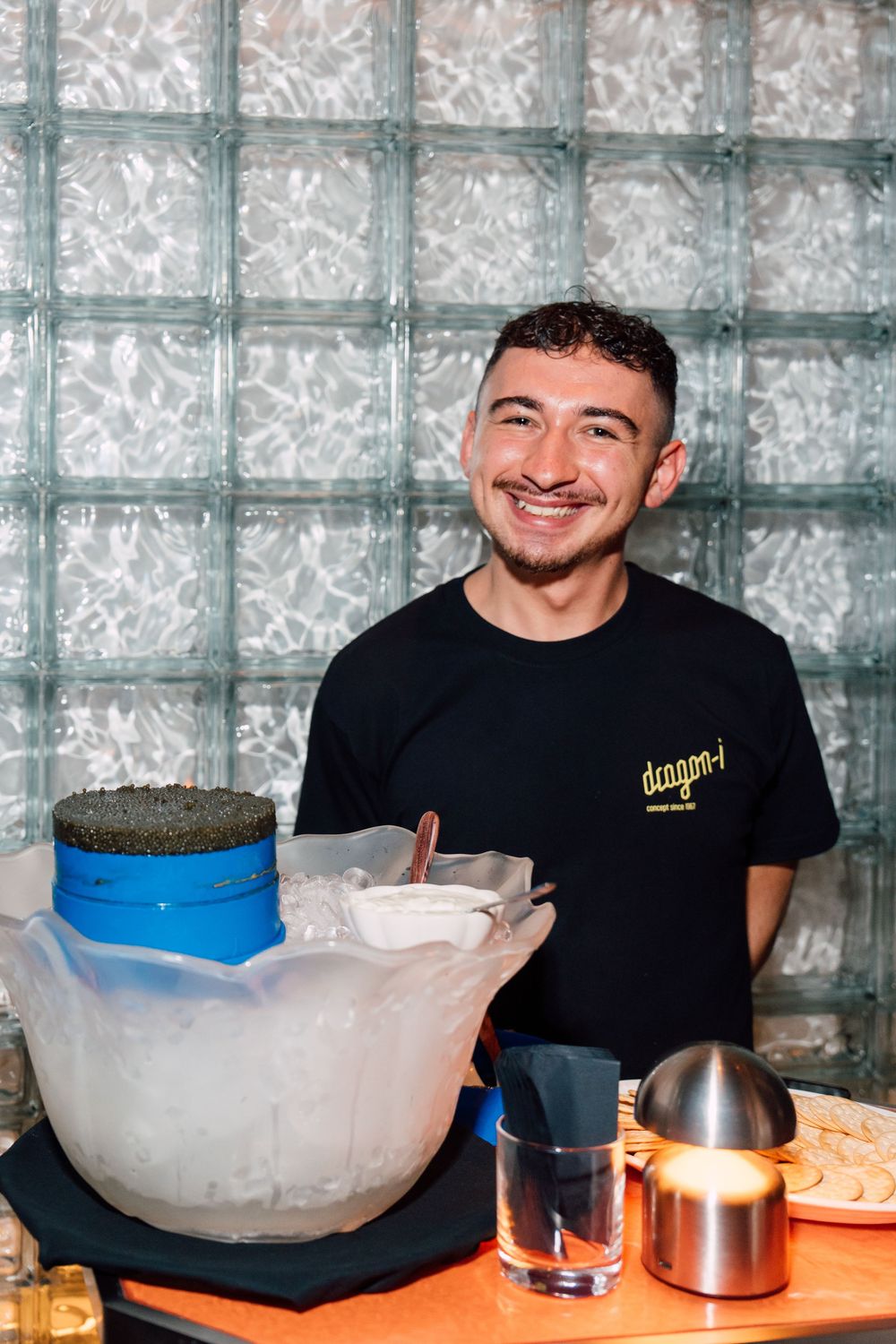 Smiling staff member at Dragon-i restaurant standing behind a bar with ice bowl and drinks and caviar in Hong Kong