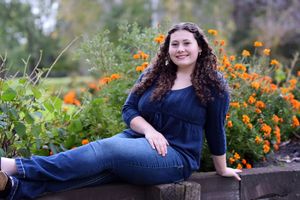 Person in navy dress reclines on wooden bench surrounded by orange flowers in garden setting.