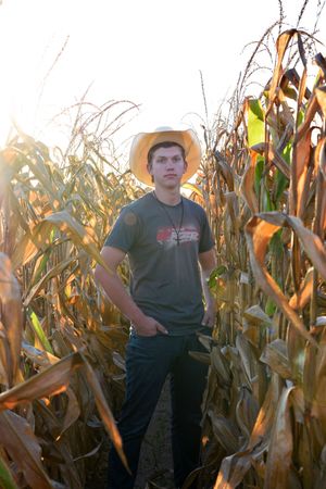 Person standing in cornfield at sunset wearing casual attire.