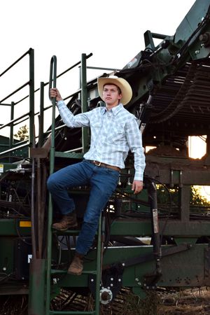 Person in western attire climbing farm equipment during sunset.