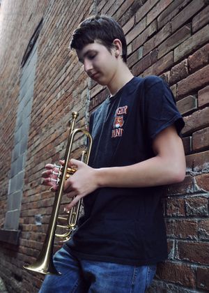 Person playing trumpet against brick wall in casual attire.