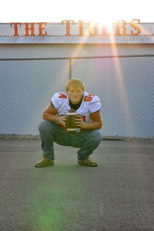 Football player crouching with ball in front of 'The Titans' sign at sunset.