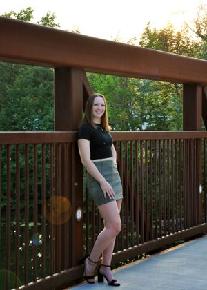 Person posing on wooden deck railing during outdoor photo session.