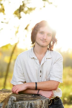 Portrait against rustic wood with golden sunlight filtering through trees.