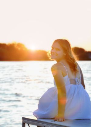 Person in white dress sitting by water during golden hour sunset.