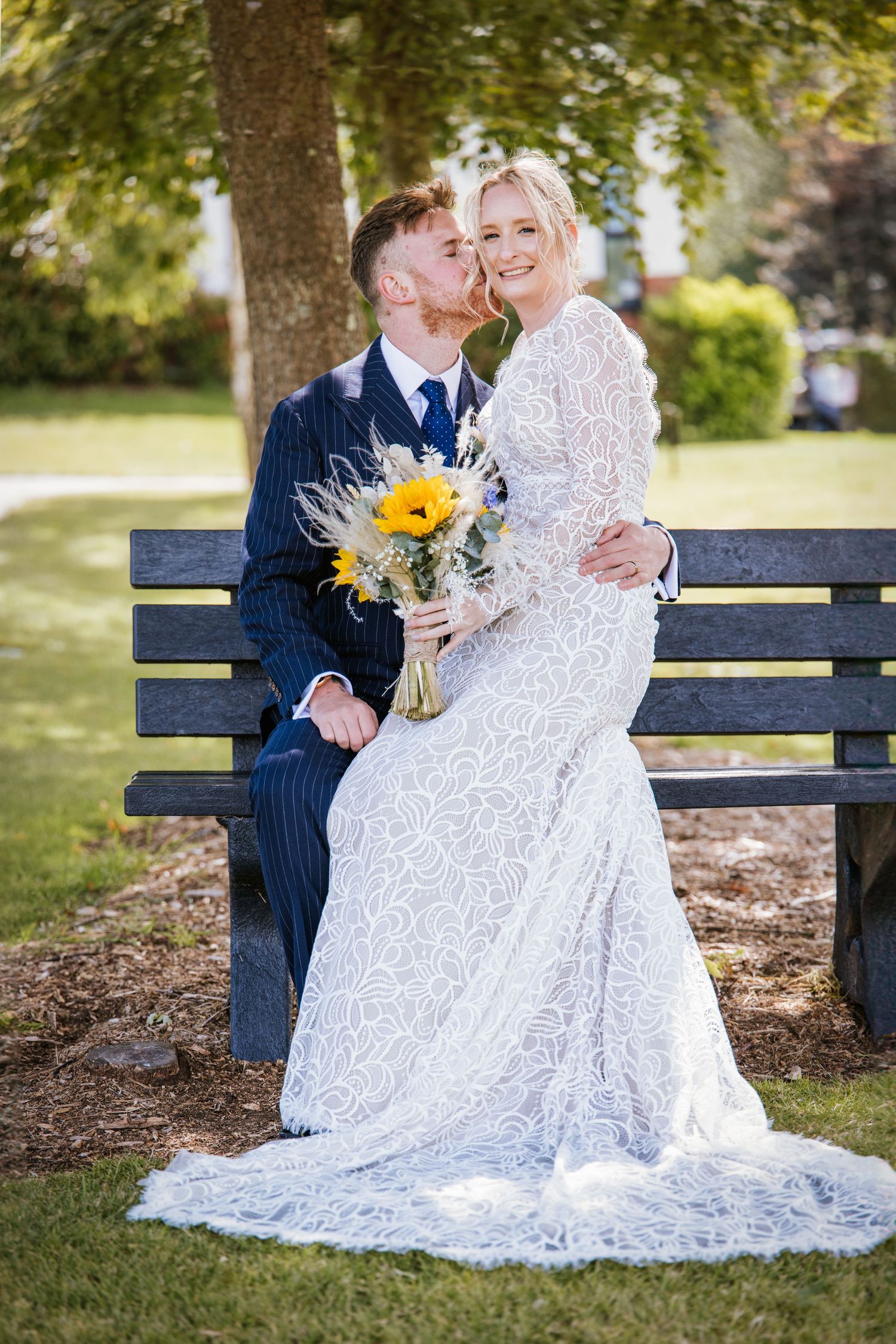 Groom kissing his bride who sits on his lap, they are on a bench at Skylark Golf Club, captured by Sylvia Patchell Photo