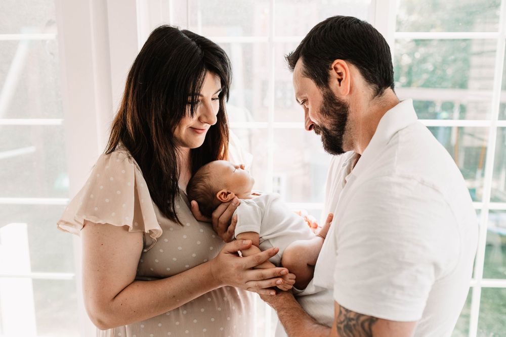Happy couple holding and smiling at newborn baby during intimate lifestyle photography session at home.