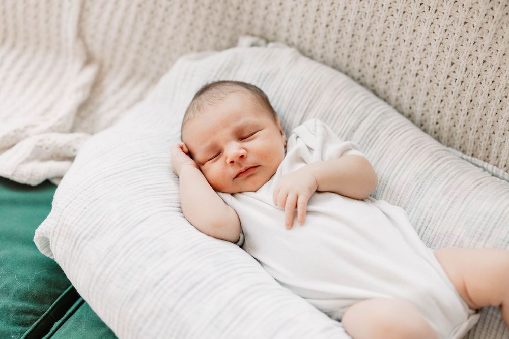 Peaceful newborn baby sleeping soundly on white bedding in natural light.