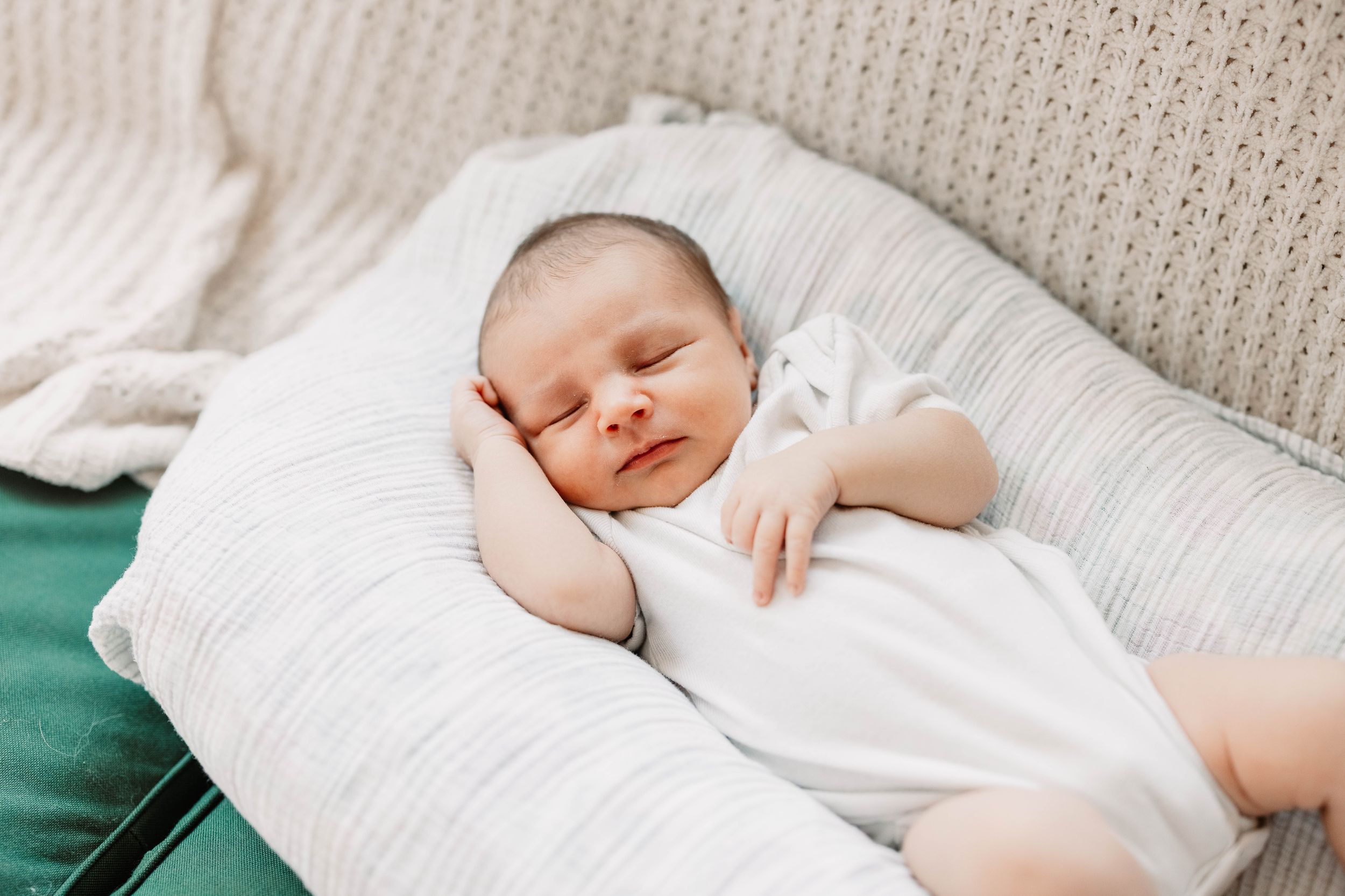 Peaceful newborn baby sleeping soundly on white bedding in natural light.