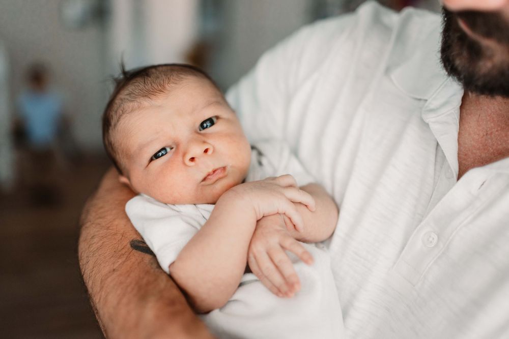 Adorable infant rests on white sheets while being gently cradled.