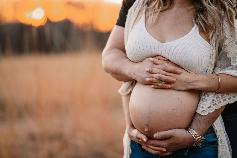 Close-up shot of expectant parents' hands cradling baby bump during sunset photoshoot.