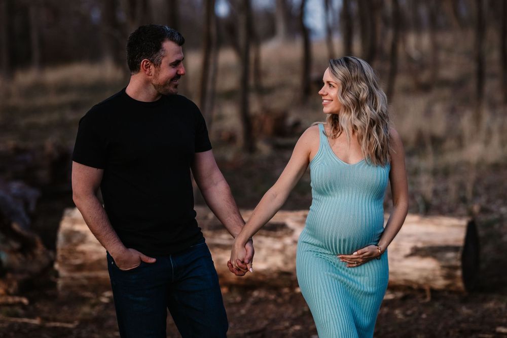 Couple holding hands during maternity shoot in forest with turquoise dress.