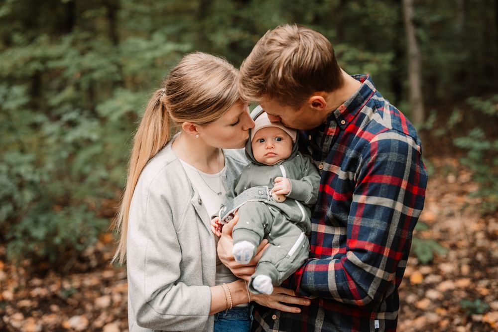 Family shares intimate moment with baby in autumn forest setting.