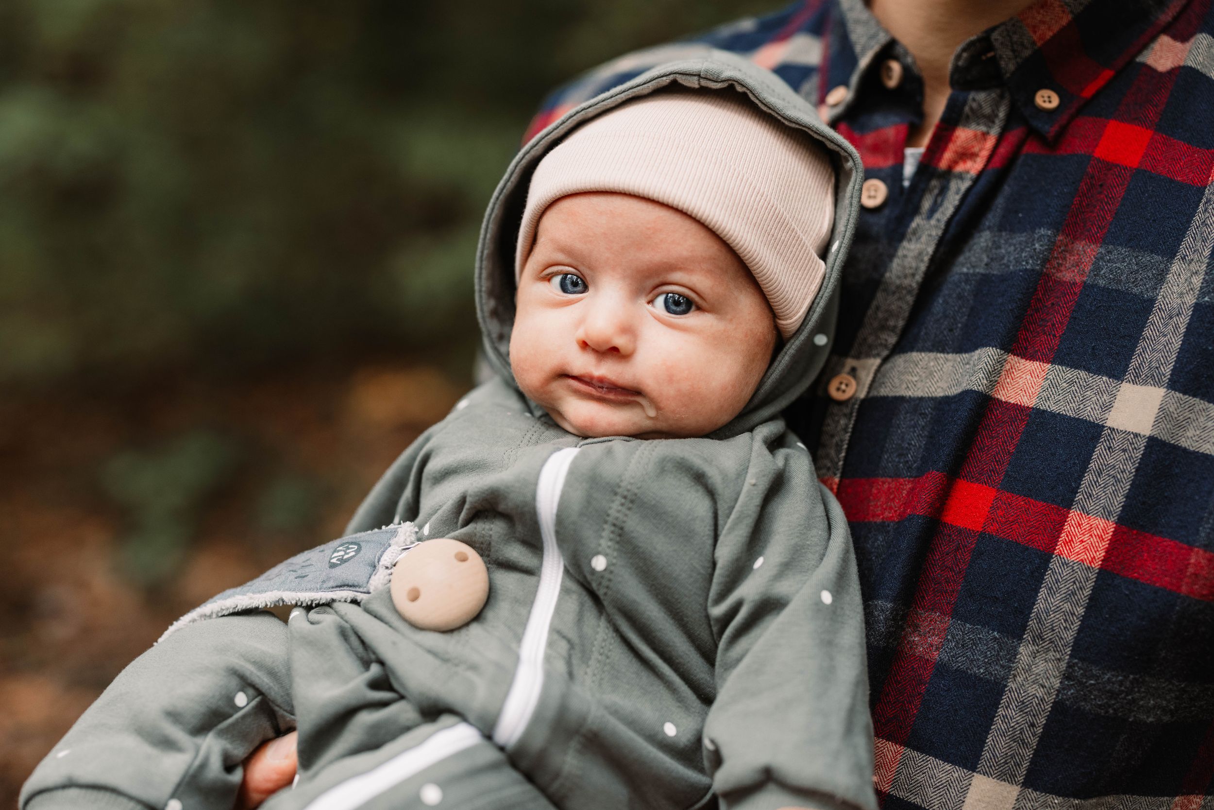 Baby wearing grey hoodie looks adorably at camera while being held.