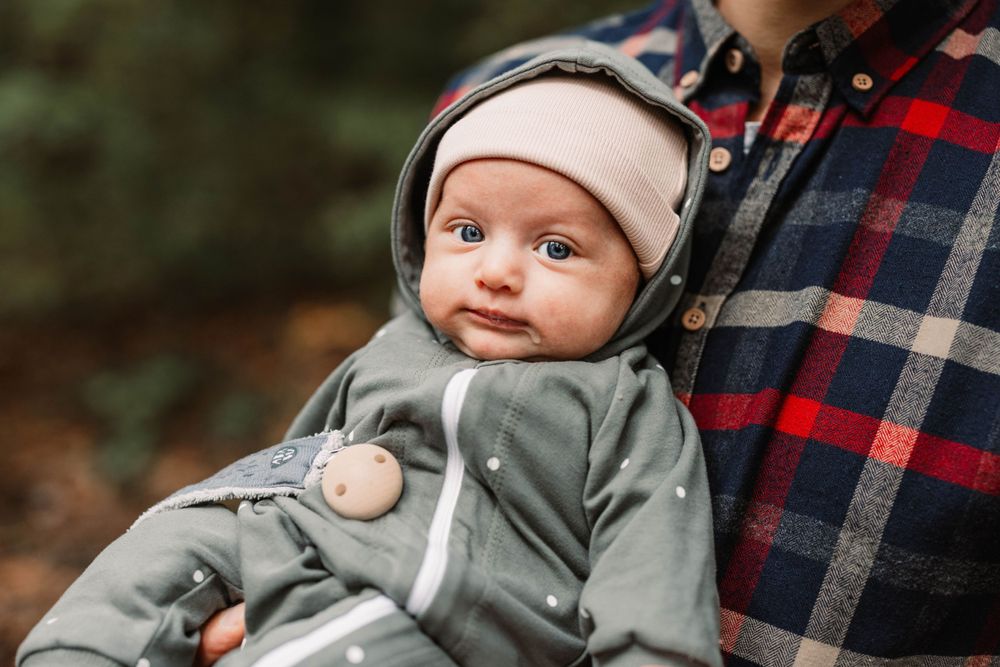 Baby wearing grey hoodie looks adorably at camera while being held.