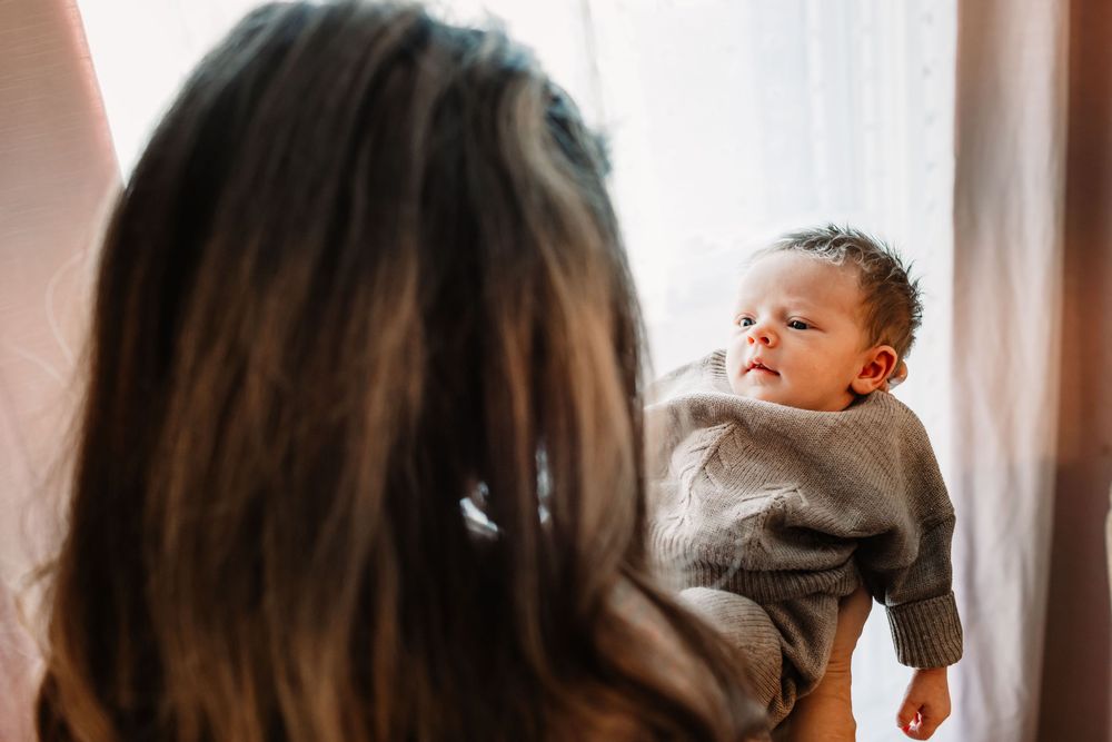 Four generations of a family show connection and love in a warm window lighting scene.