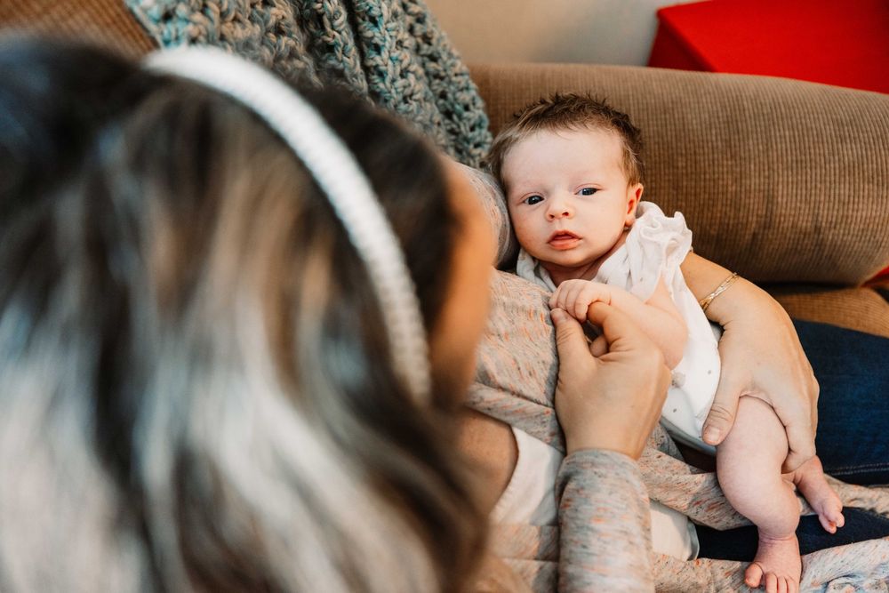 A tender moment between a parent and infant sitting on a gray sofa while surrounded by holiday decor.
