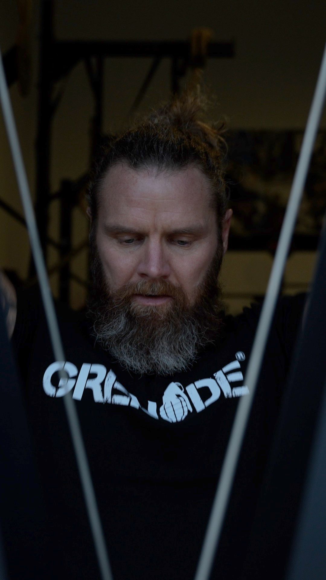 Close-up portrait of person in Grenade shirt with fitness equipment in background.