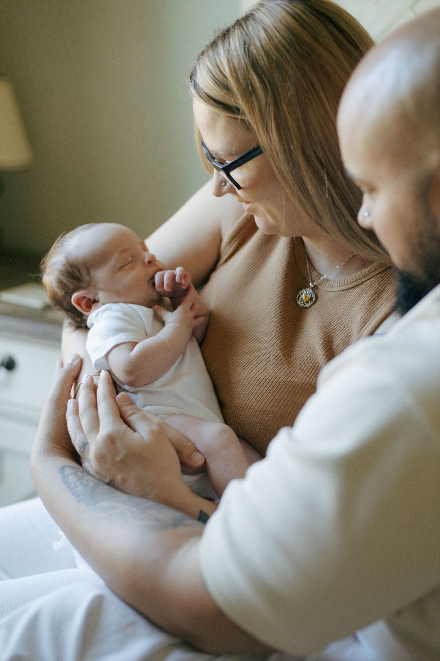 An intimate moment as a tiny newborn yawns while being tenderly cradled by adults in a softly lit room.