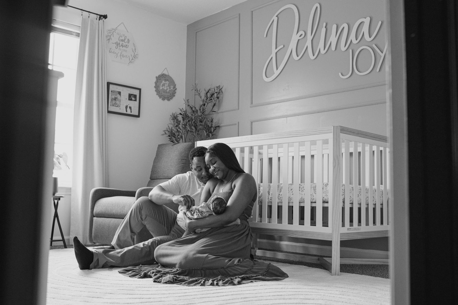 Black and white nursery scene with a parent and baby relaxing by a crib.