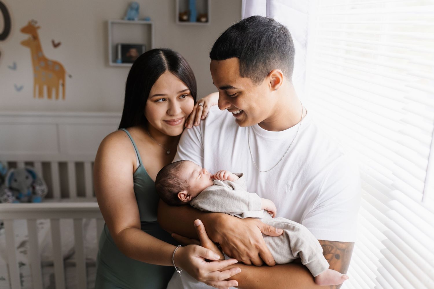 Parents holding their newborn baby in a nursery decorated with giraffe wall art.
