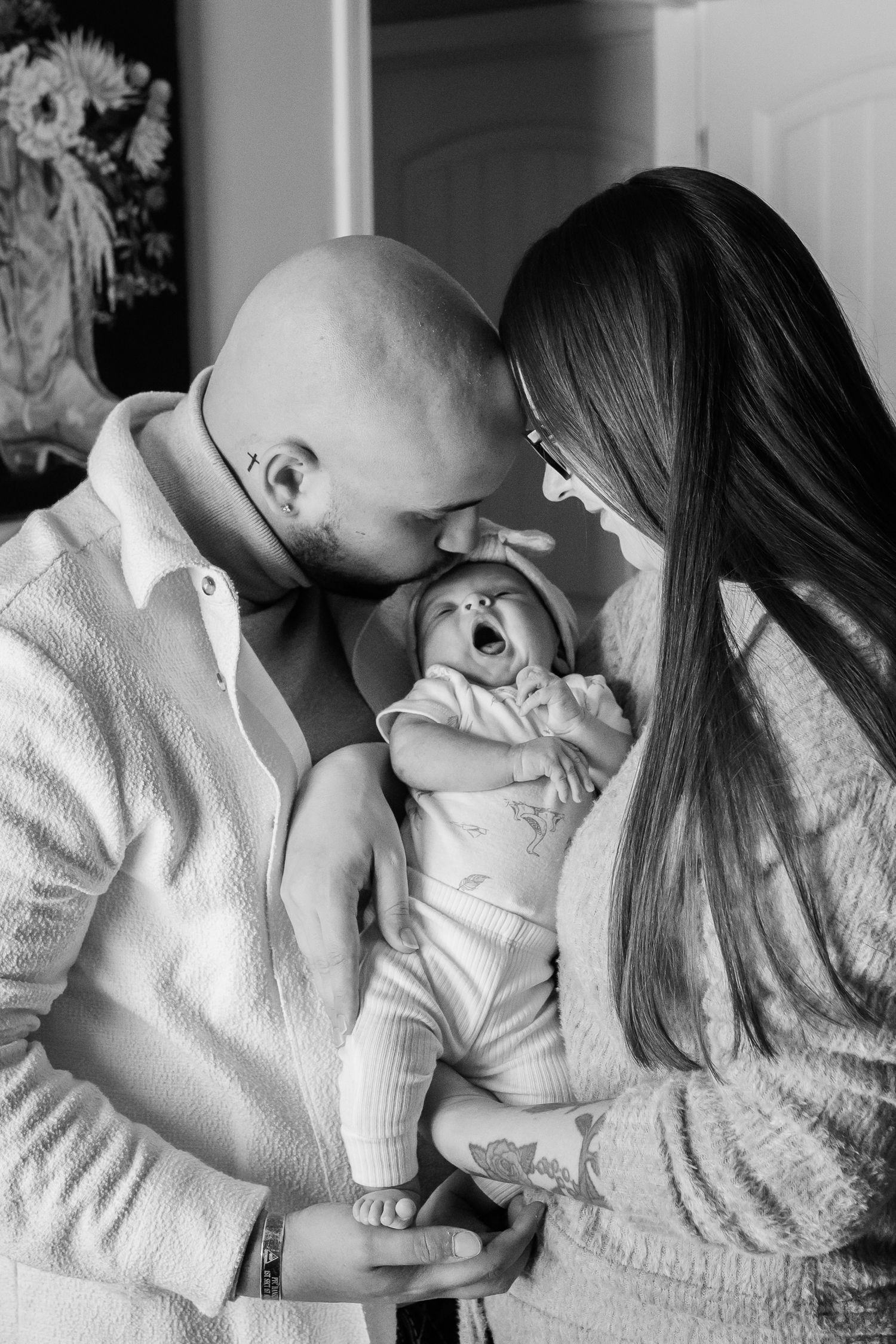 Intimate black and white portrait of parents sharing a tender moment with their yawning newborn.