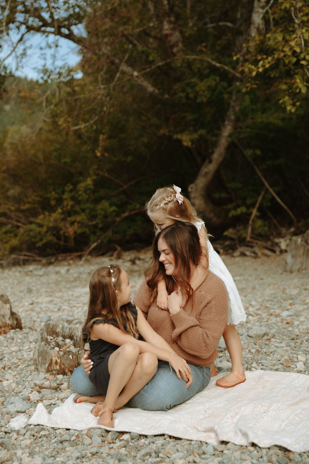 A candid outdoor moment shared on a blanket by the shore during golden hour with trees in the background.