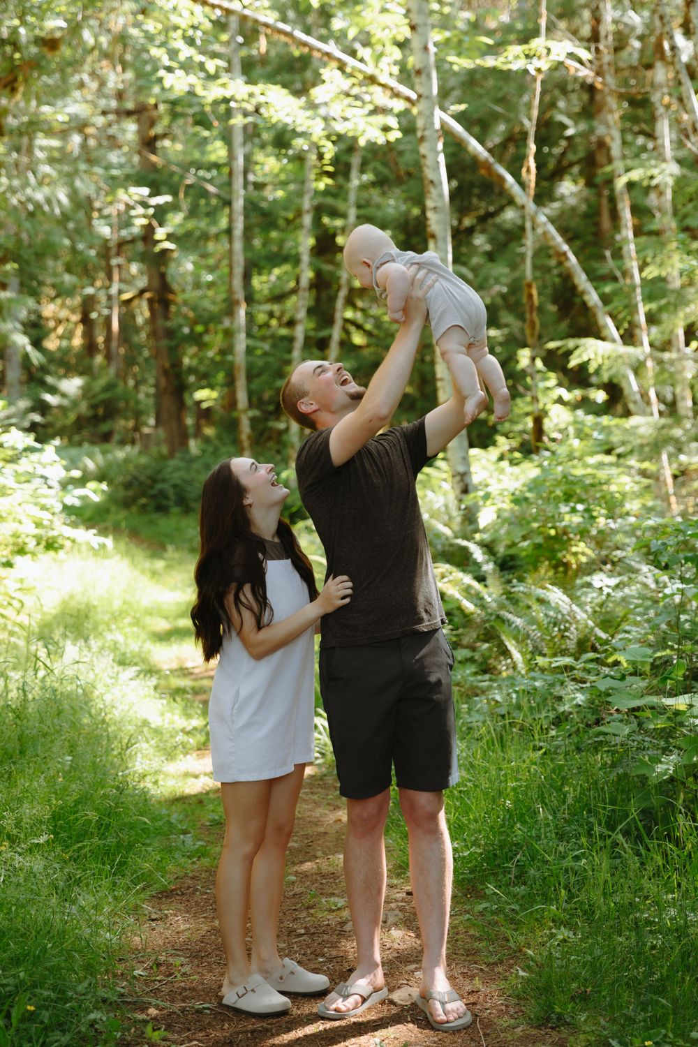 Family enjoying a playful moment together on a sunlit forest trail surrounded by lush green foliage.