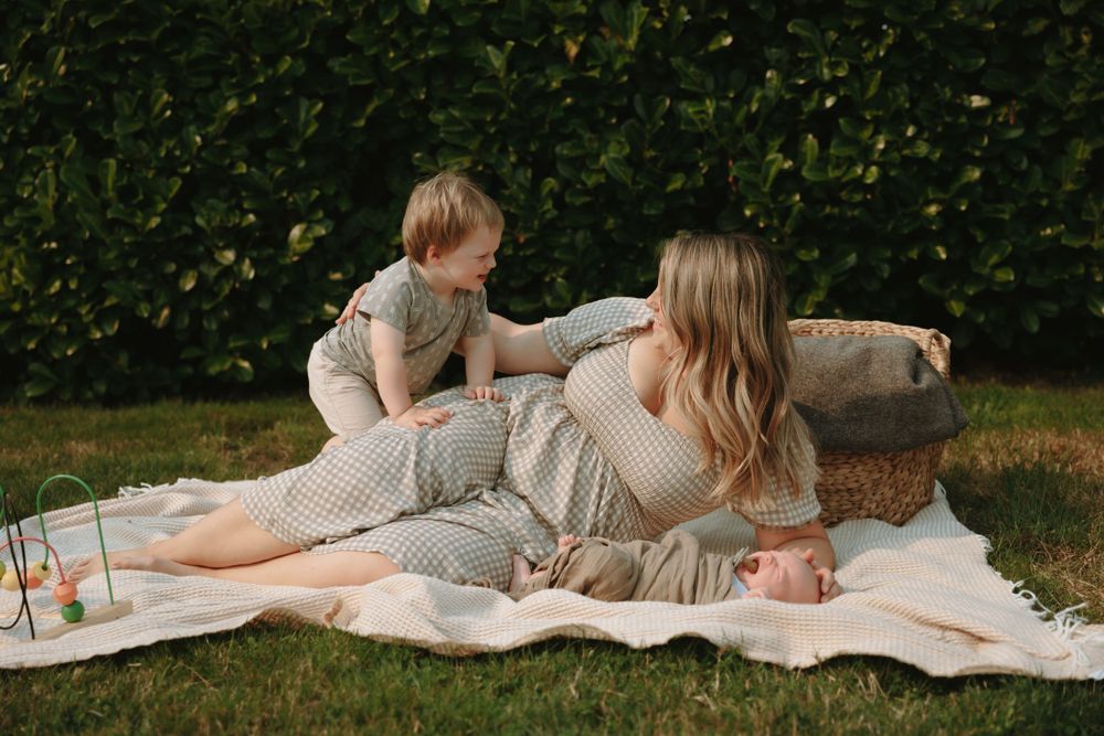 A family enjoys a relaxing picnic on a white blanket on their lawn with green hedges in the background.