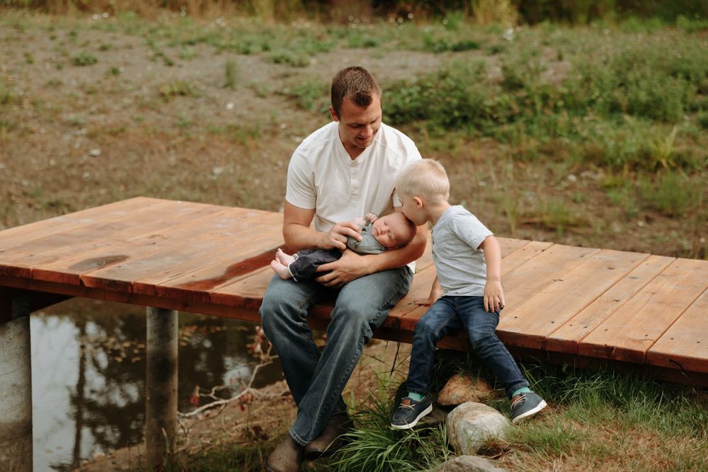 Two people sitting together on a wooden deck by a pond having a tender moment outdoors.