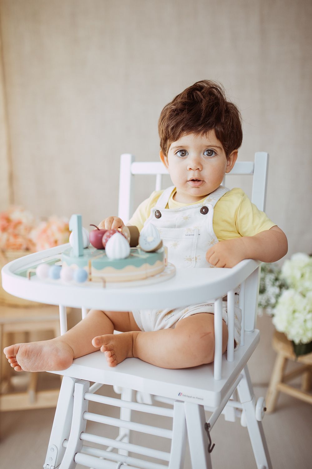 Baby in white high chair reaching for birthday decorations on table.