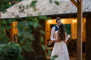 Bride and groom share intimate dance outside warmly lit rustic wooden barn wedding venue at dusk.