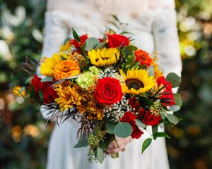 Vibrant bridal bouquet featuring sunflowers, red roses, marigolds, and eucalyptus held by bride in white gown.