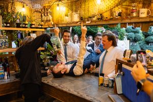 Groomsmen celebrate wildly at rustic bar during wedding reception with drinks and laughter.