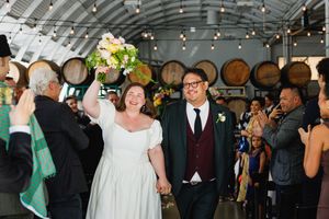 Newlywed couple walks joyfully down the aisle at a rustic winery wedding reception.