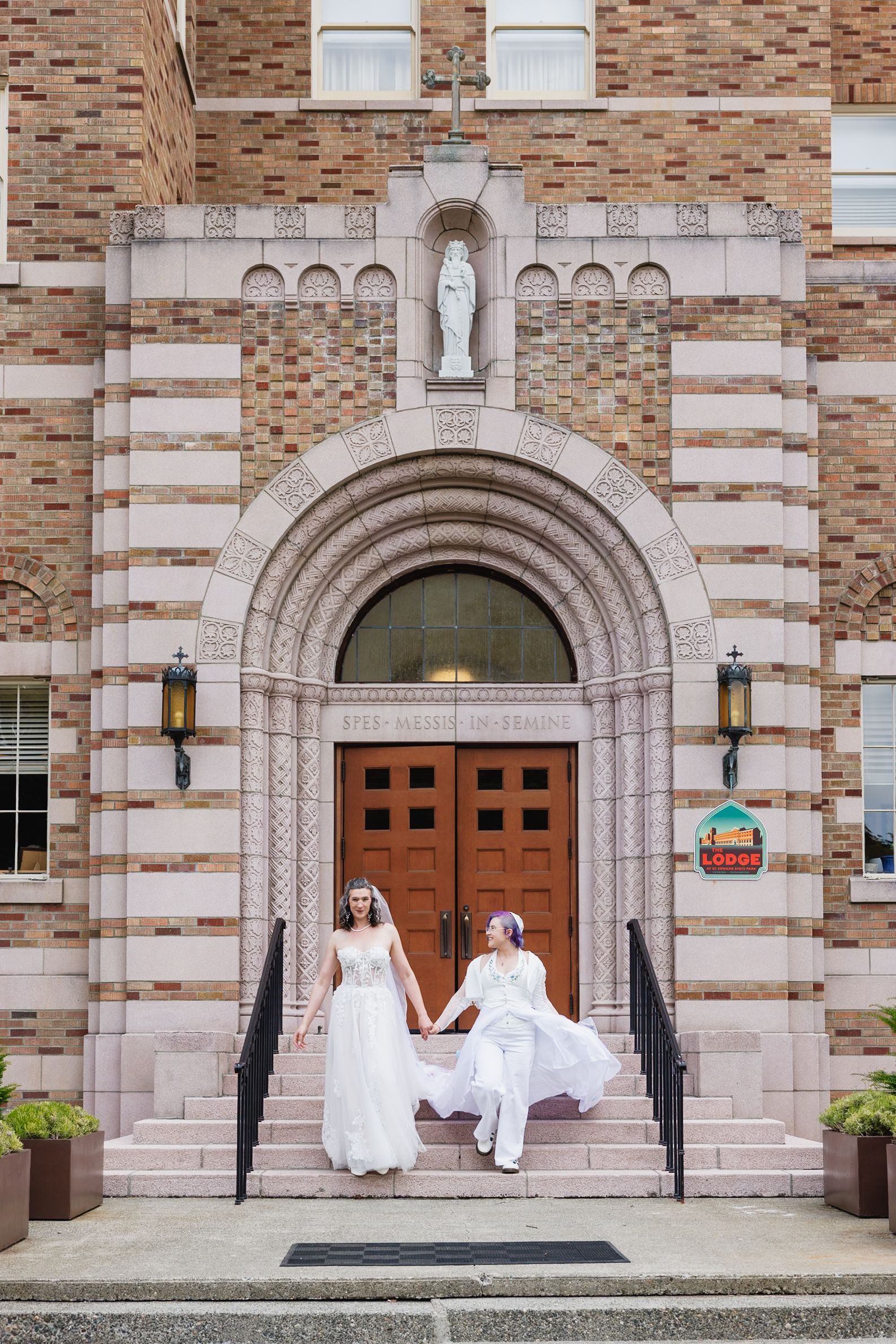 Two brides hold hands descending steps of a historic brick building after their wedding ceremony.