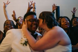 Two brides share a first kiss surrounded by cheering guests at their wedding reception.