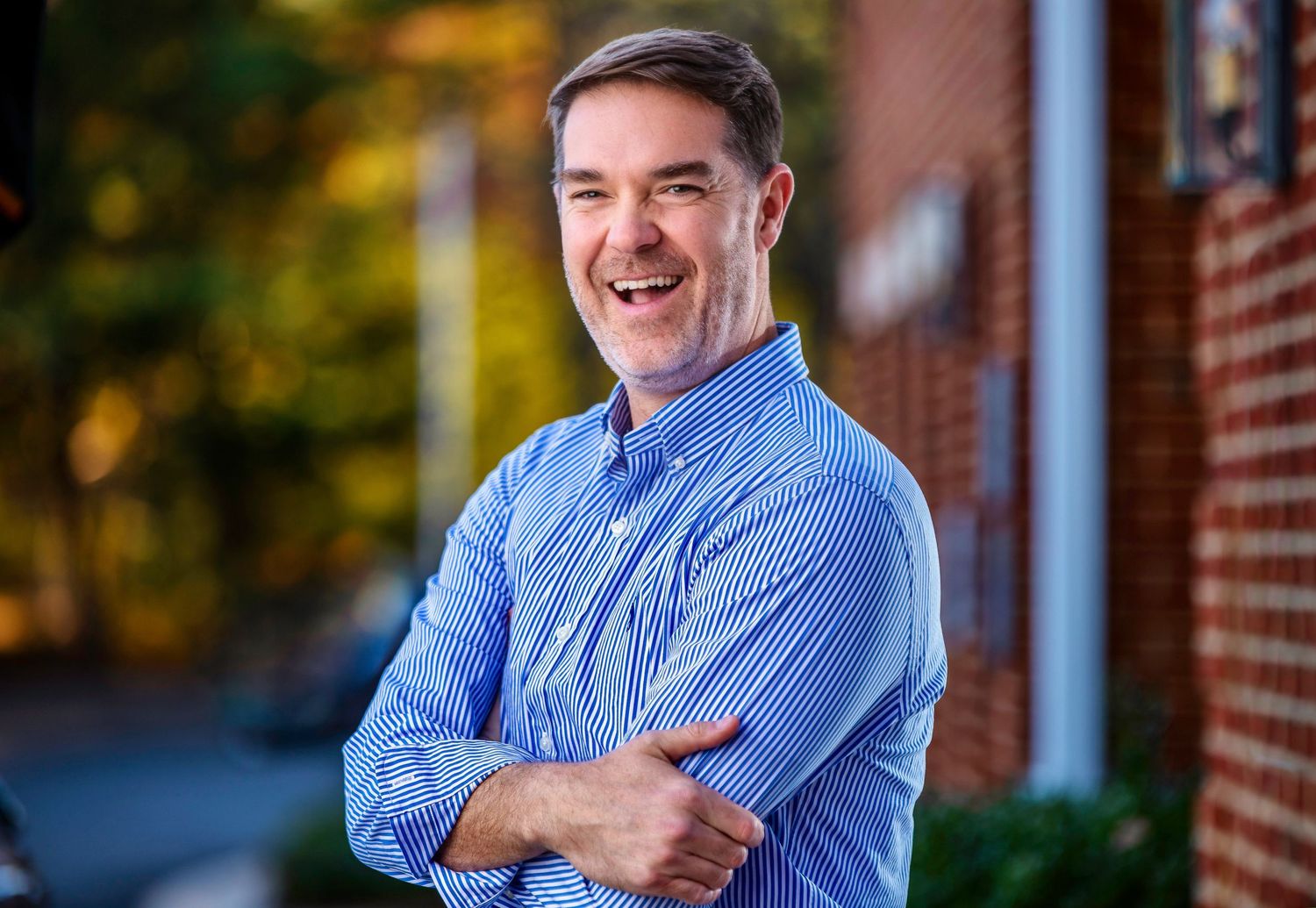 Portrait of person in blue striped button-down shirt against autumn backdrop.