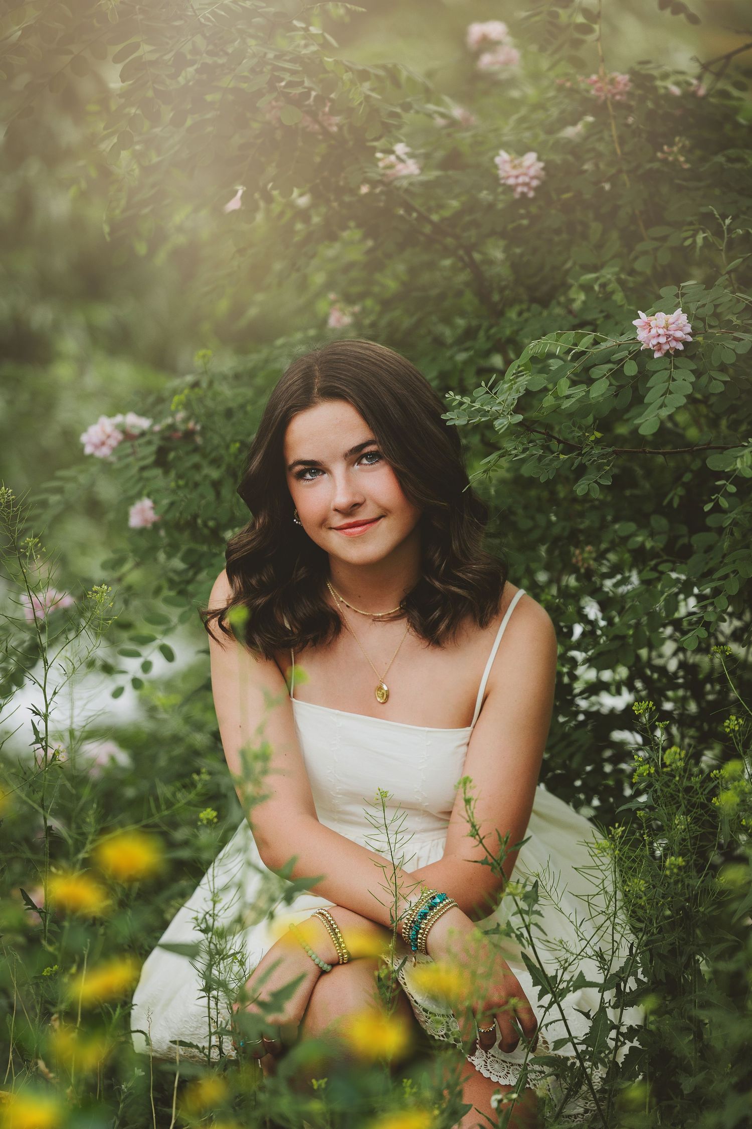 A dreamy portrait in a garden setting with white dress among pink flowers and lush greenery in soft natural lighting.