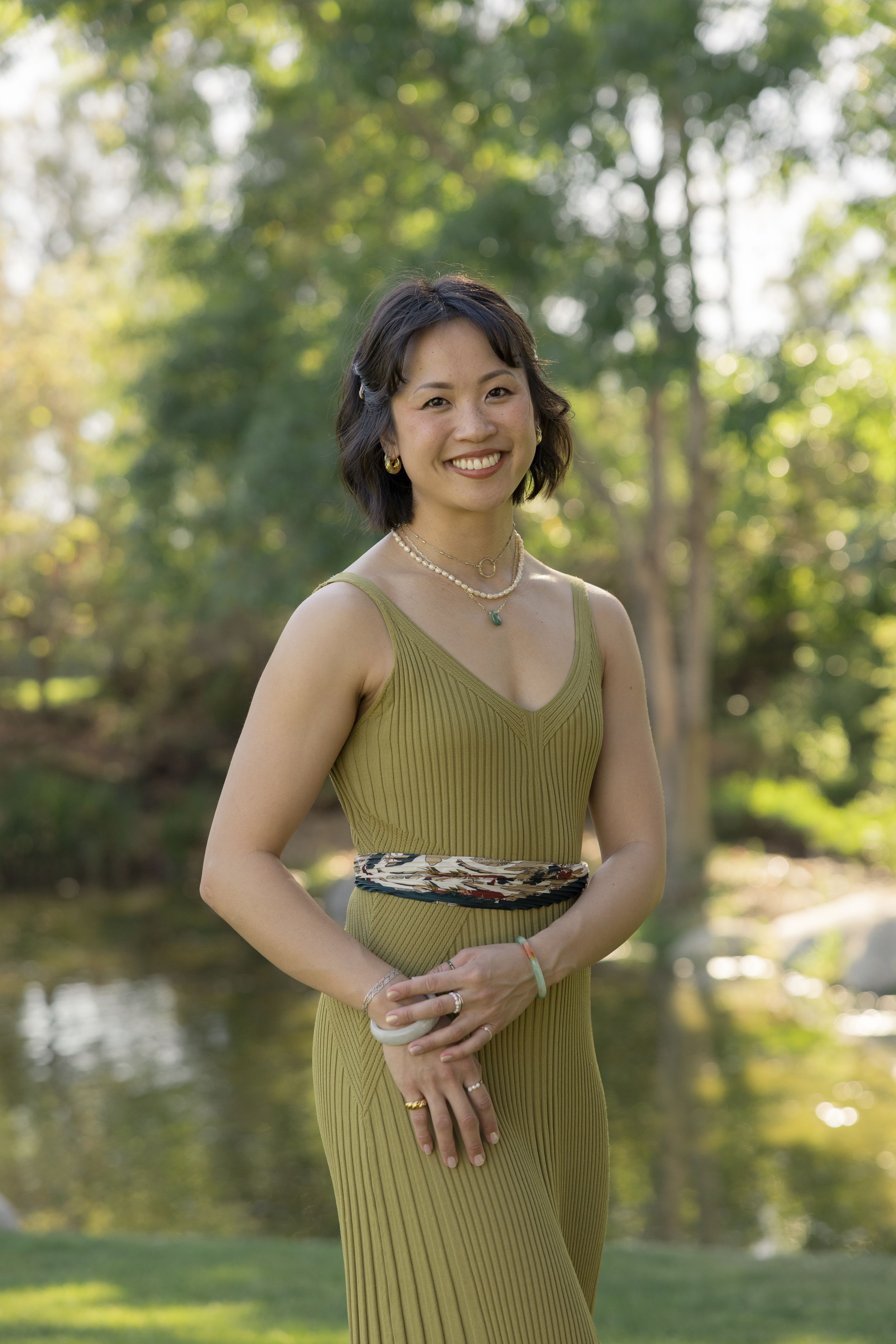 Portrait of woman in white top sitting beside pampas grass decor against neutral background.