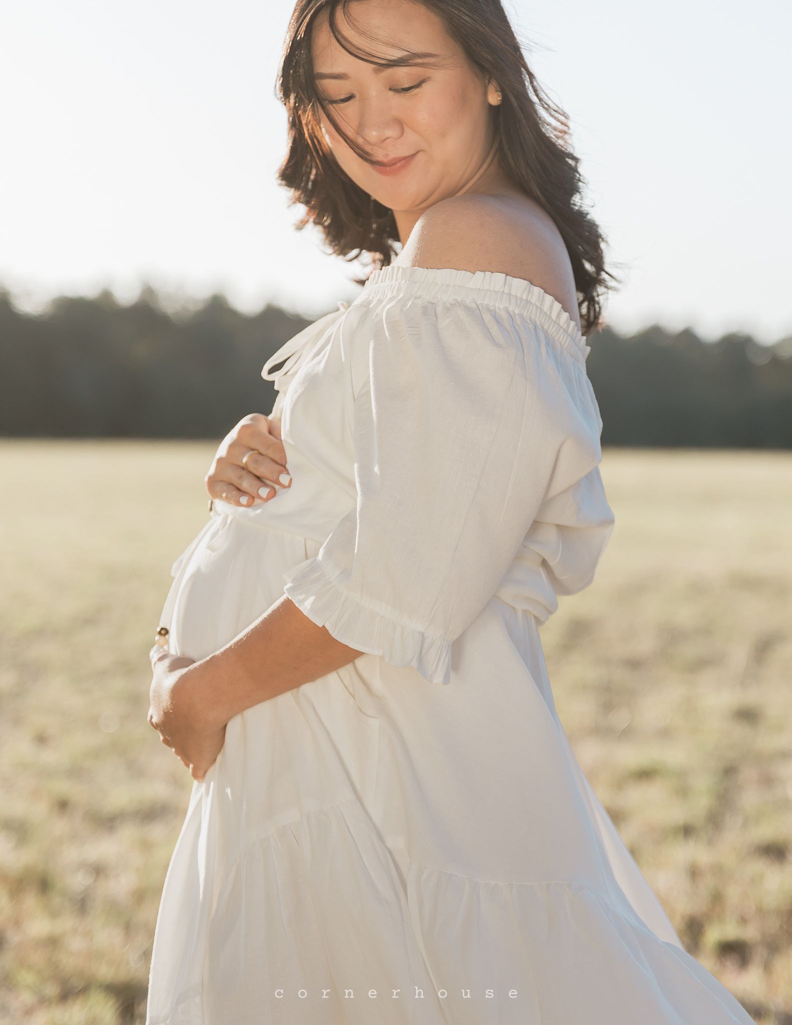 A flowing white dress gracefully billows in the breeze as someone stands in a golden wheat field at sunset.