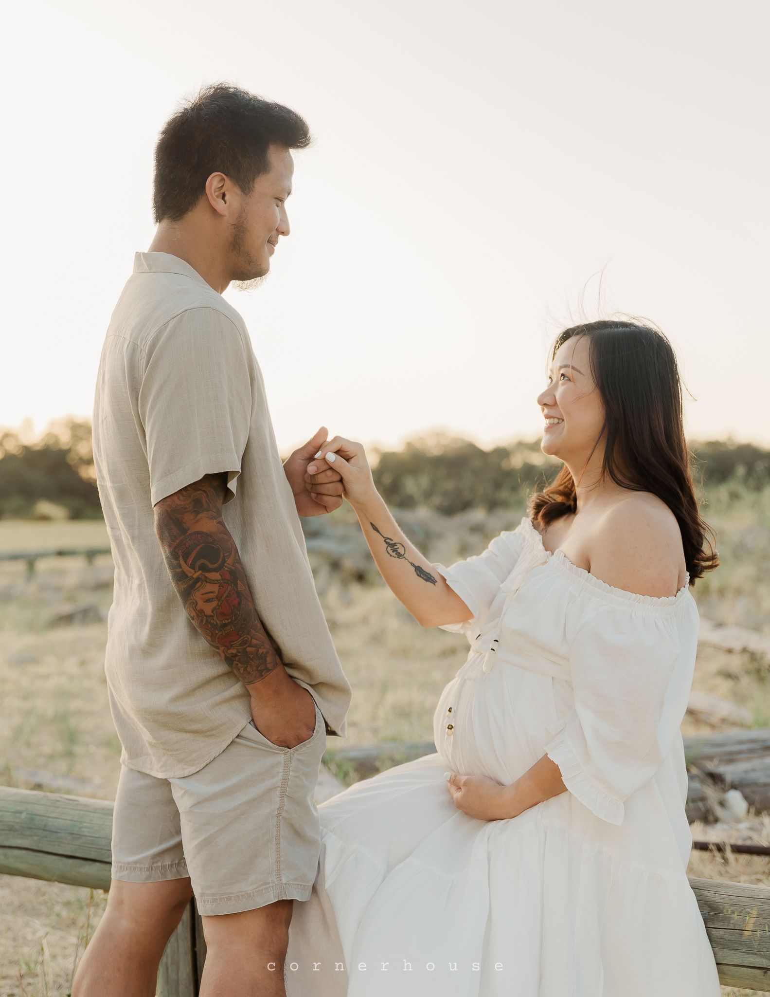 A loving couple shares tender moments at sunset in matching cream-colored outfits on a grassy field.