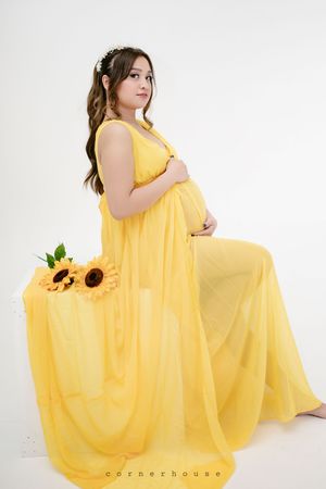 A yellow flowing maternity gown is showcased in multiple elegant poses against a white studio backdrop.