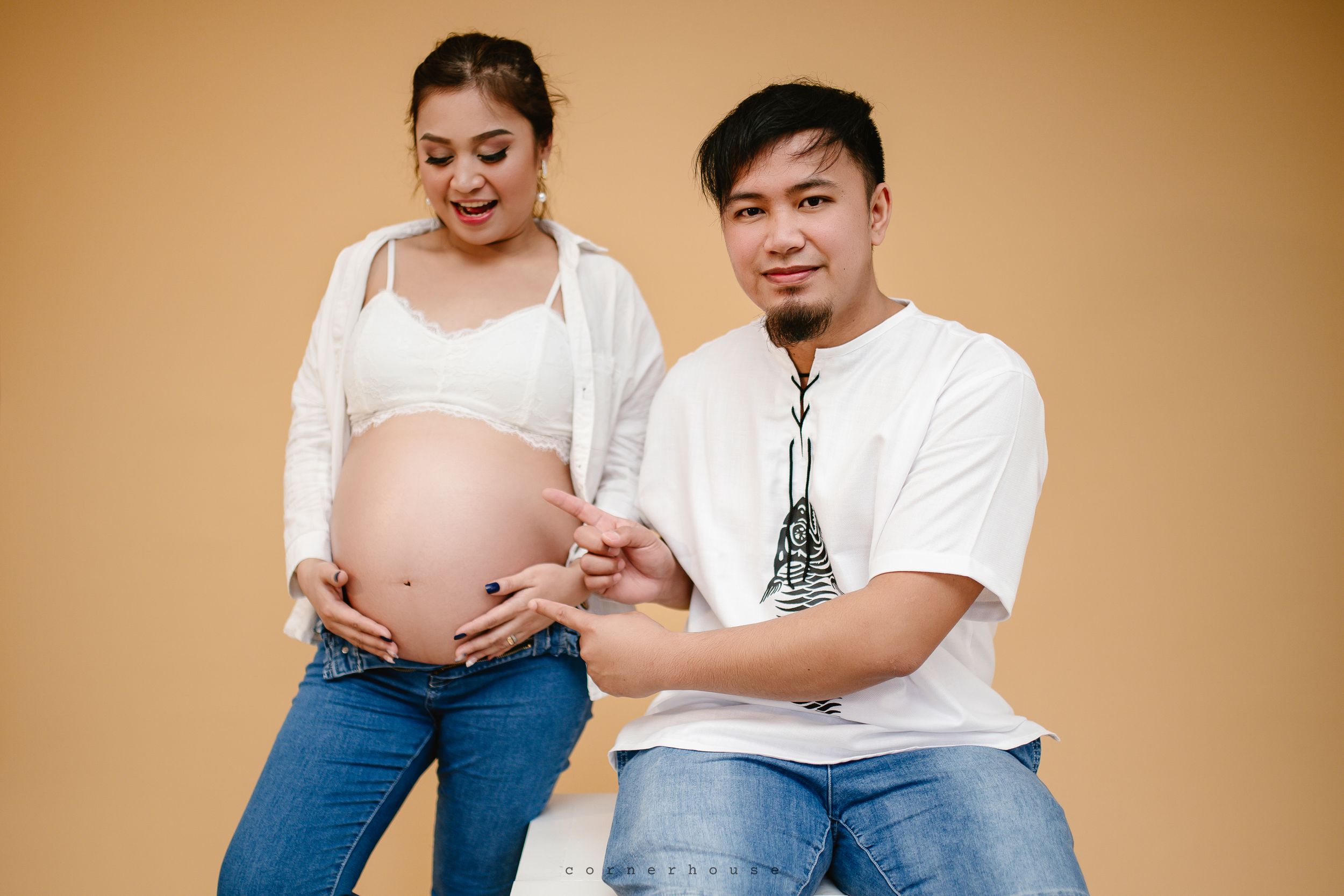 A pregnancy photography series showing parents looking joyfully at their growing baby bump in warm brown studio setting.