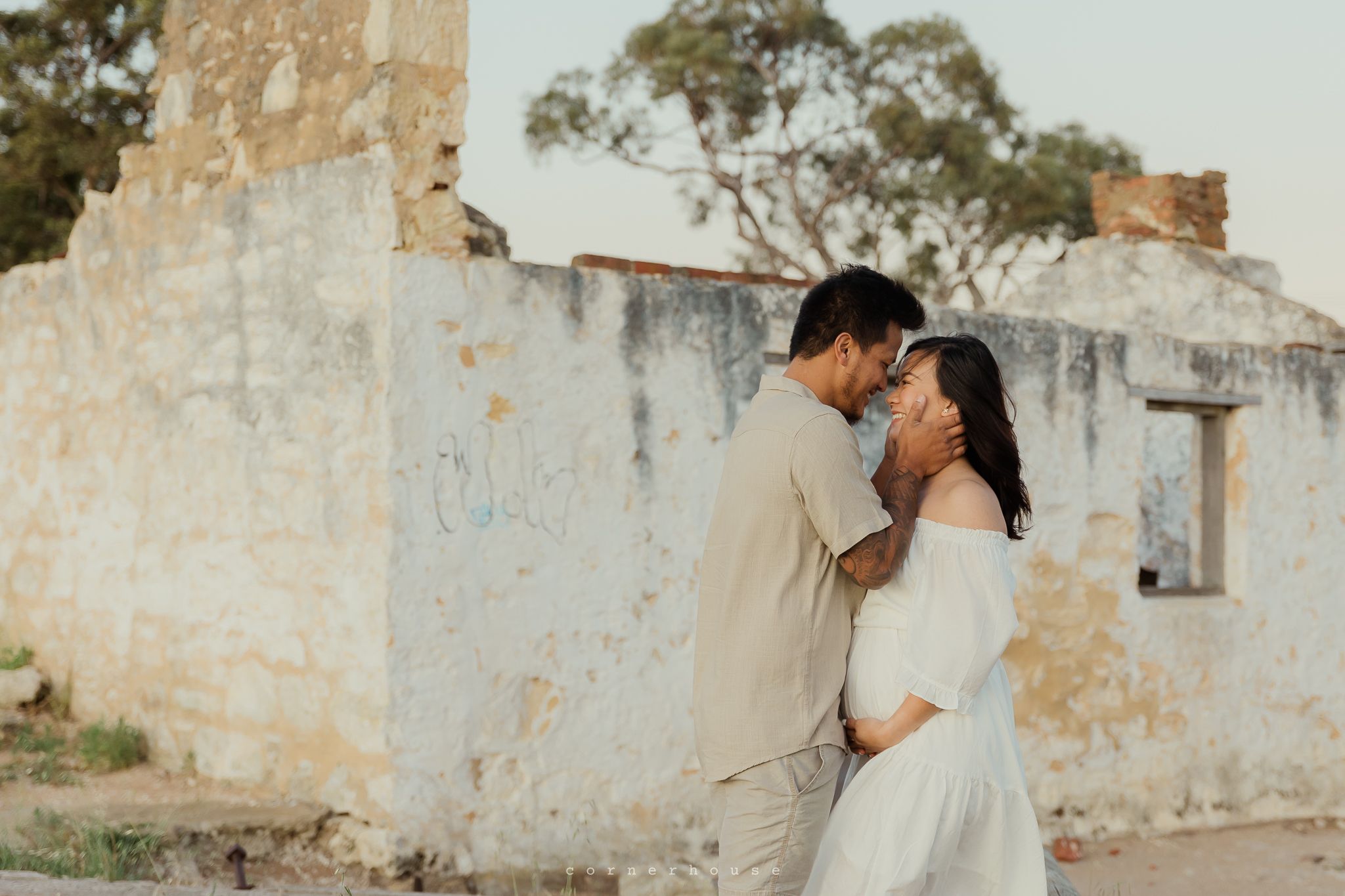 Couple in traditional wedding attire share tender moments against rustic stone walls in a romantic photoshoot.
