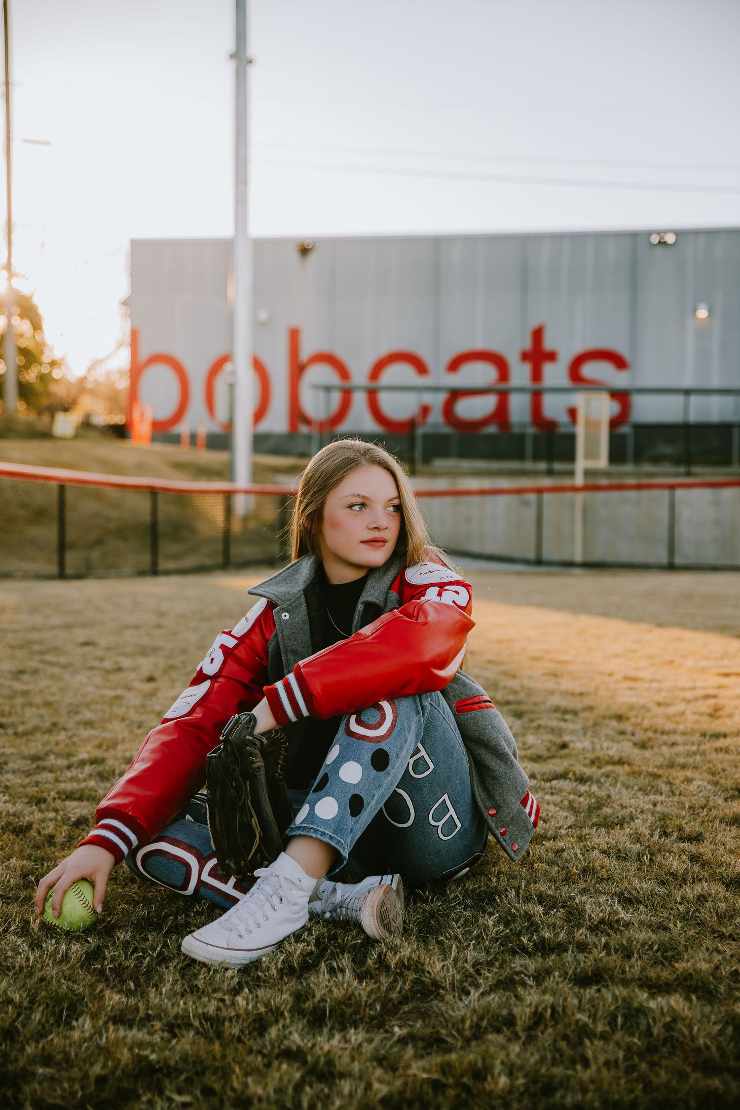 Senior portrait session with athlete in red jersey on sports field at sunset.