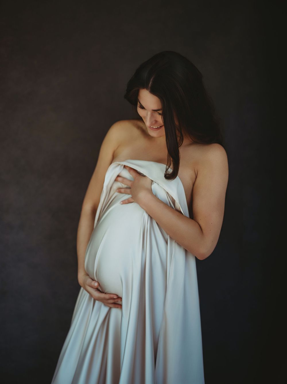 Artistic maternity photo series showing woman in flowing white fabric against dark background in four sequential poses - Bellevue WA
