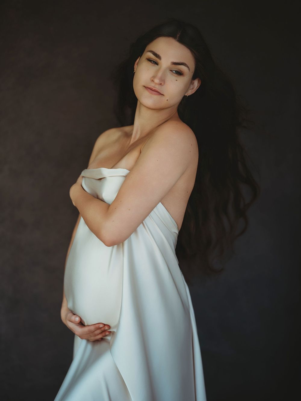 A series of elegant portrait photos showing someone in a flowing white dress against a dark background - maternity photography Bellevue WA
