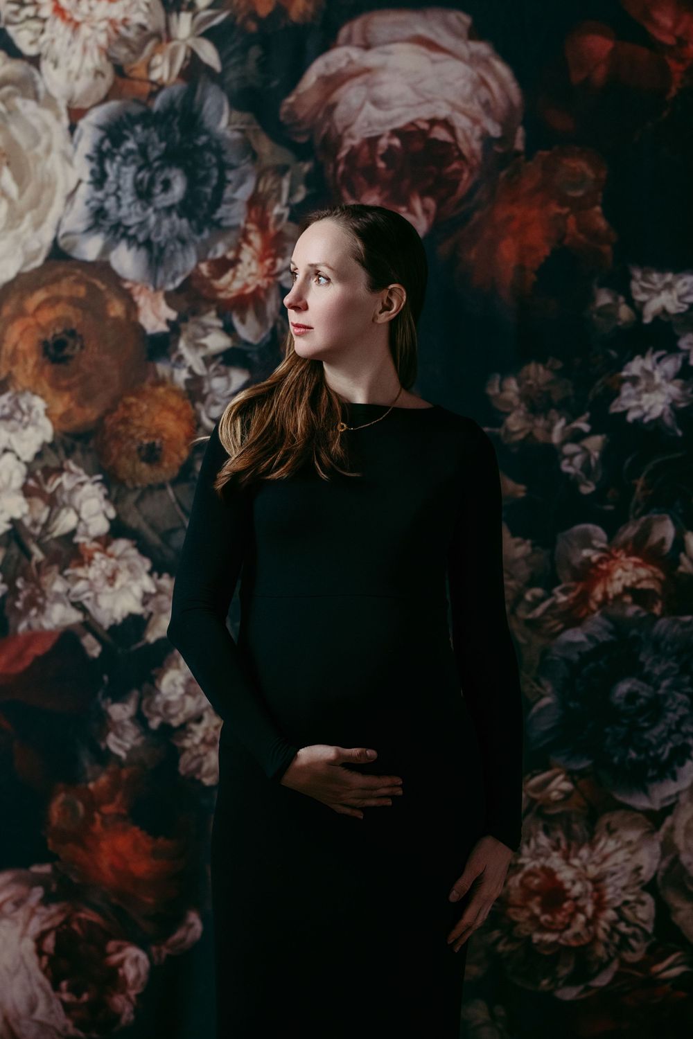 A woman in black stands against a dramatic floral wallpaper backdrop. Bellevue studio, WA